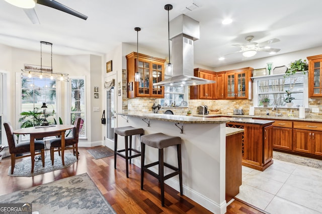 kitchen with a breakfast bar, ceiling fan, island range hood, and brown cabinetry