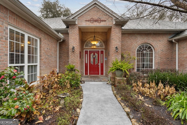 property entrance with a shingled roof and brick siding