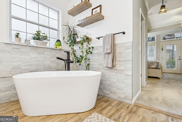 bathroom featuring a freestanding tub, wainscoting, tile walls, and wood finished floors