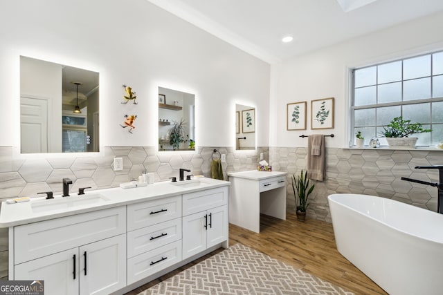 bathroom with double vanity, a freestanding bath, tile walls, and a sink