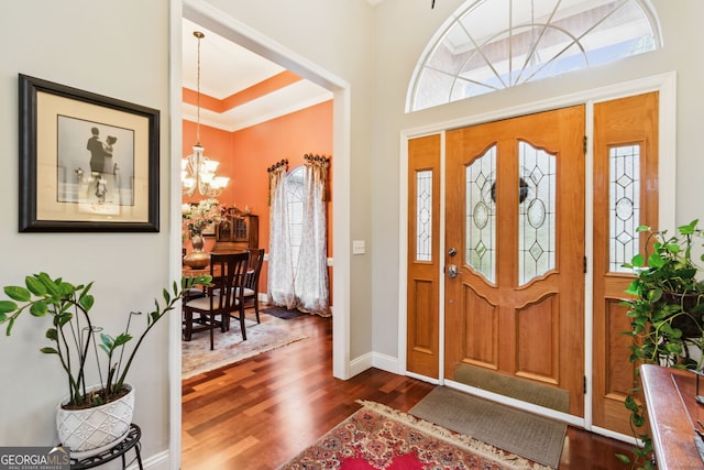 foyer with a tray ceiling, dark wood-type flooring, ornamental molding, a chandelier, and baseboards