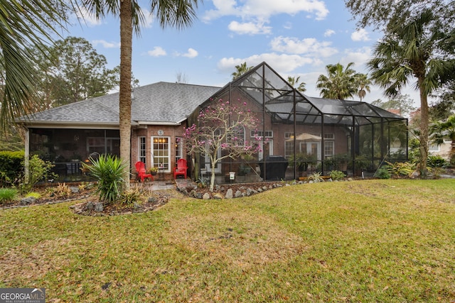 rear view of property with a shingled roof, a lanai, brick siding, and a yard