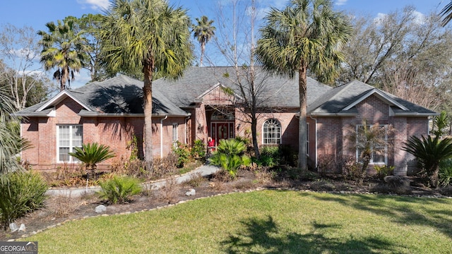 single story home featuring roof with shingles, a front yard, and brick siding