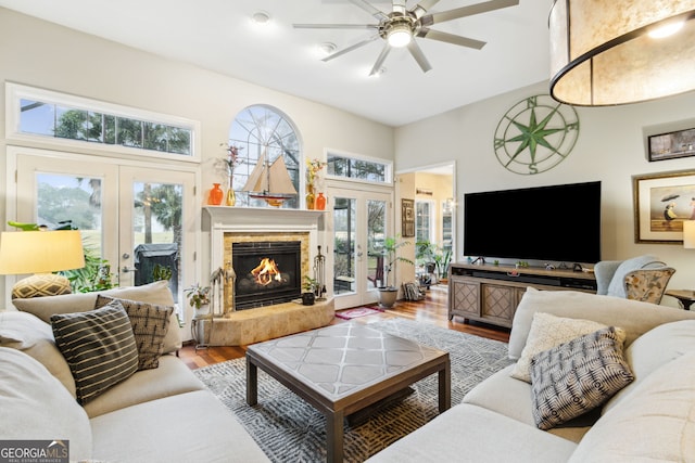 living area with french doors, wood finished floors, a glass covered fireplace, and a ceiling fan