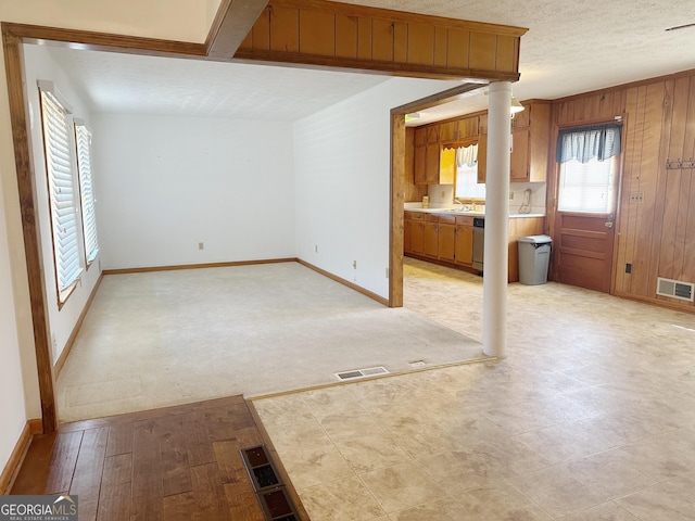 unfurnished living room with a textured ceiling, visible vents, and wooden walls