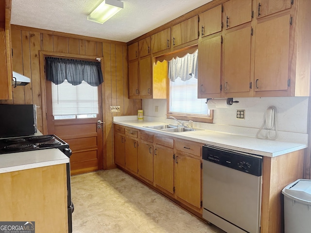 kitchen featuring light countertops, stainless steel dishwasher, wood walls, a sink, and under cabinet range hood