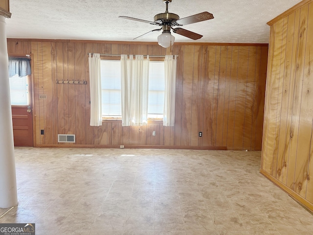 spare room featuring ceiling fan, wood walls, a textured ceiling, and visible vents