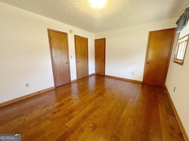 unfurnished bedroom with multiple closets, a textured ceiling, baseboards, and hardwood / wood-style floors