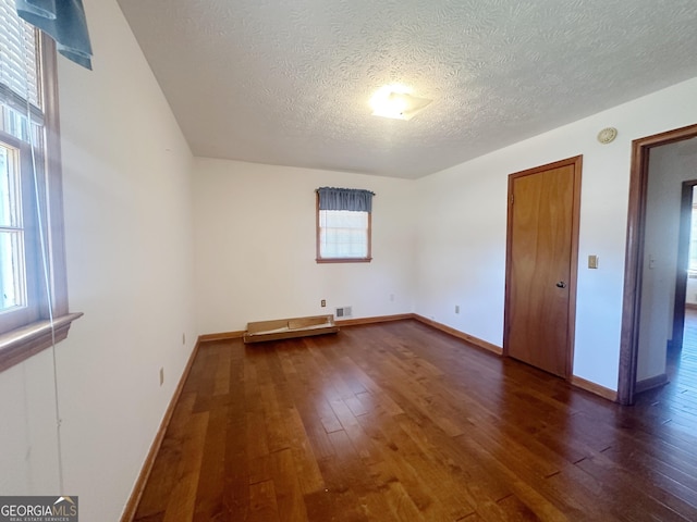 unfurnished bedroom with baseboards, a textured ceiling, visible vents, and dark wood-style flooring