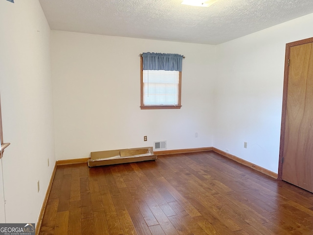 unfurnished room with wood-type flooring, visible vents, and a textured ceiling