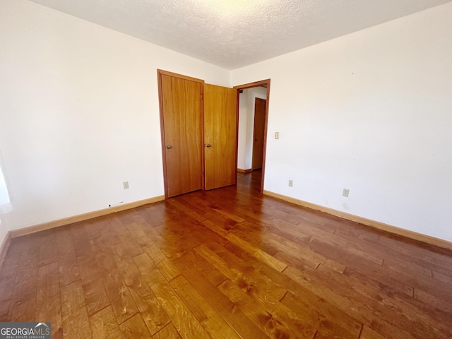 empty room featuring wood-type flooring, a textured ceiling, and baseboards