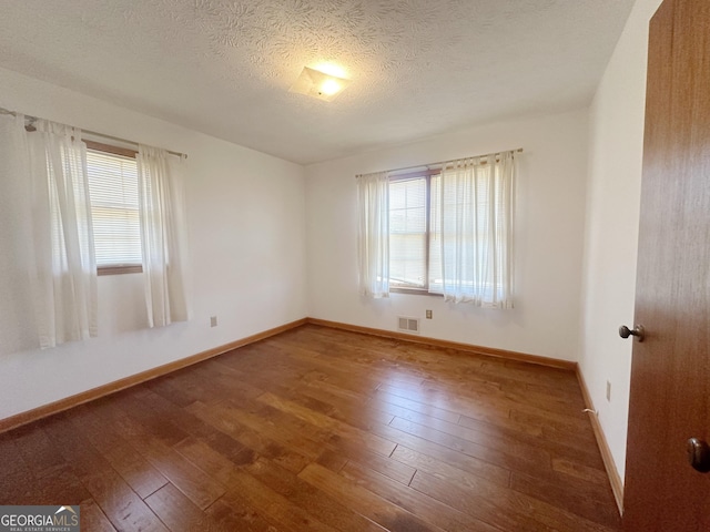 empty room with visible vents, a textured ceiling, hardwood / wood-style flooring, and baseboards