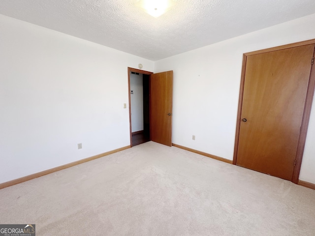 unfurnished bedroom featuring light colored carpet, a textured ceiling, and baseboards