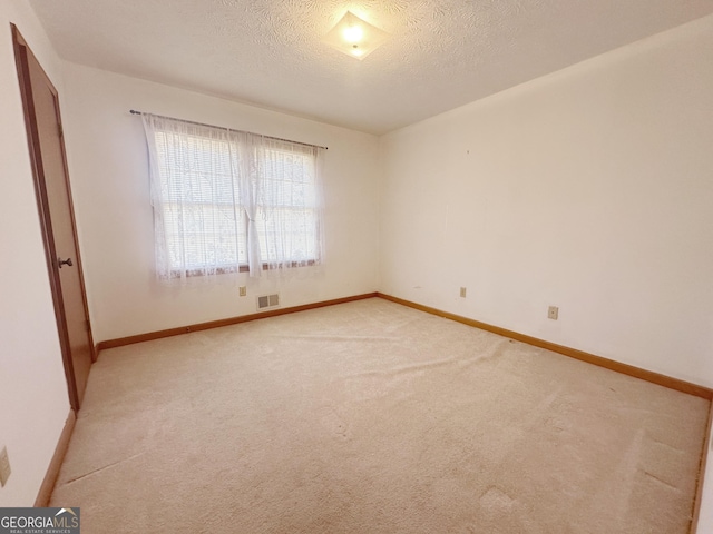 spare room featuring light colored carpet, visible vents, a textured ceiling, and baseboards