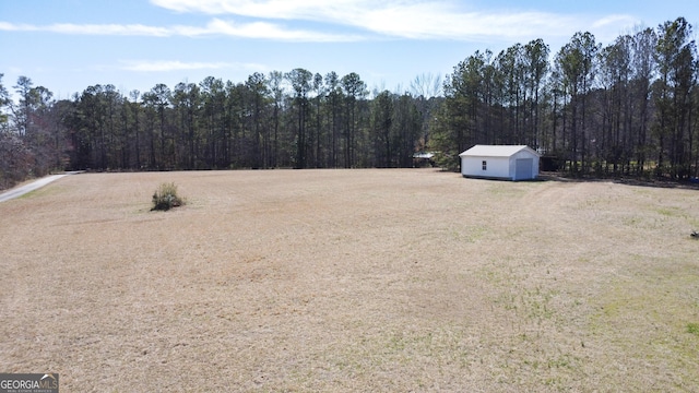 view of yard with a garage, a view of trees, and an outdoor structure