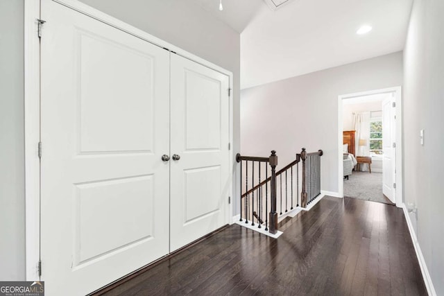 hall with dark wood-type flooring, baseboards, and an upstairs landing