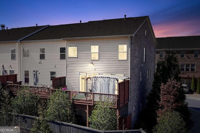 back of property at dusk featuring brick siding and a wooden deck