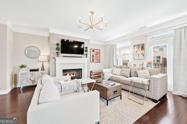 living room with dark wood finished floors, visible vents, an inviting chandelier, ornamental molding, and a warm lit fireplace