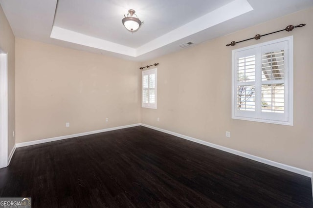 empty room featuring a raised ceiling, visible vents, dark wood finished floors, and baseboards