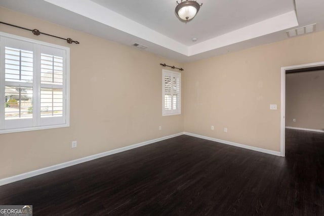 empty room featuring a raised ceiling, visible vents, baseboards, and wood finished floors