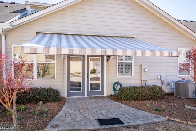 entrance to property with a shingled roof and central AC unit