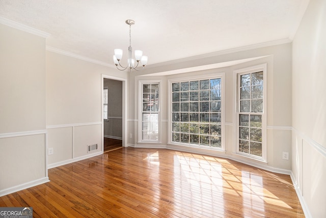 unfurnished dining area with visible vents, a decorative wall, an inviting chandelier, light wood-style floors, and ornamental molding