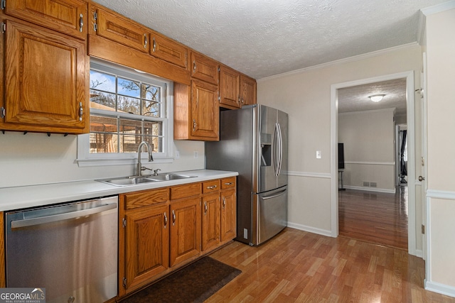 kitchen with light wood finished floors, appliances with stainless steel finishes, brown cabinets, light countertops, and a sink