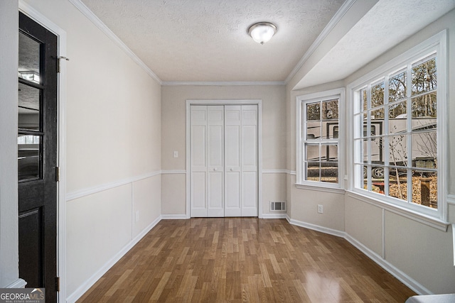 unfurnished bedroom featuring visible vents, ornamental molding, wood finished floors, a textured ceiling, and a closet