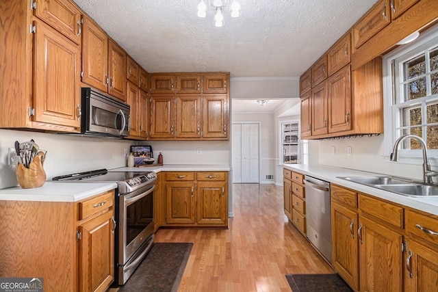 kitchen with appliances with stainless steel finishes, brown cabinetry, light wood-type flooring, and a sink