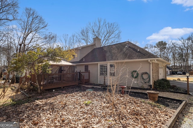 rear view of house featuring a garage, a shingled roof, a chimney, and a wooden deck