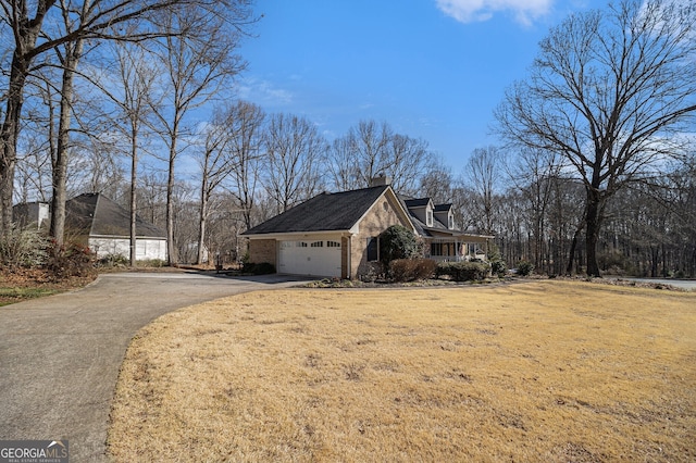 view of side of home featuring brick siding, a yard, a chimney, a garage, and driveway