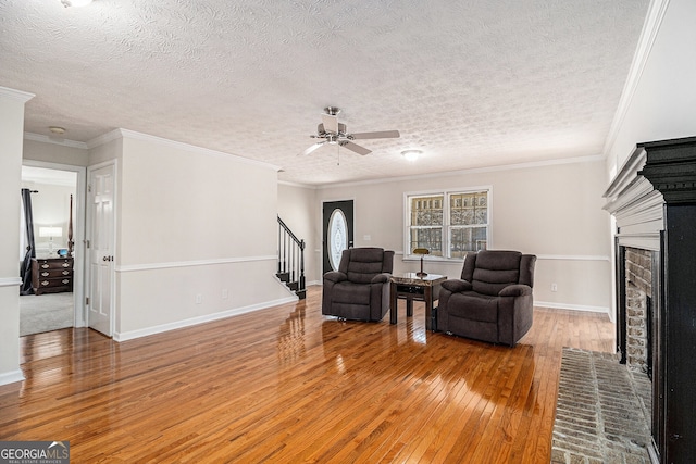 sitting room with stairway, a brick fireplace, light wood-style flooring, and crown molding