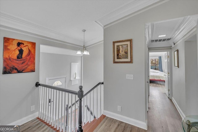 hall featuring baseboards, visible vents, wood finished floors, crown molding, and an upstairs landing