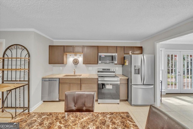 kitchen with a sink, light countertops, french doors, appliances with stainless steel finishes, and crown molding