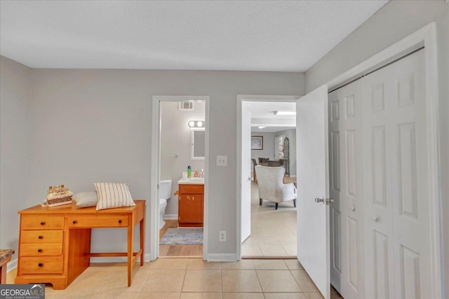 bedroom featuring ensuite bathroom, light tile patterned flooring, visible vents, baseboards, and a closet