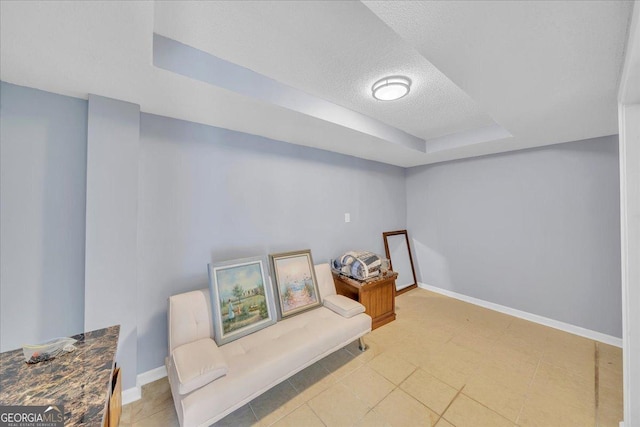 living area with a textured ceiling, a tray ceiling, and baseboards