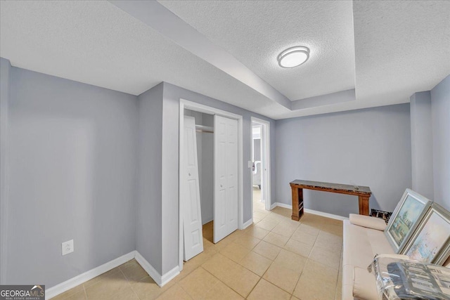 interior space with light tile patterned floors, a closet, a textured ceiling, and baseboards