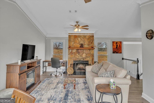 living area with crown molding, a ceiling fan, wood finished floors, and a stone fireplace