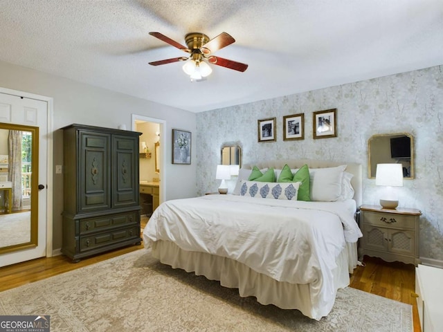 bedroom featuring a textured ceiling, wood finished floors, and wallpapered walls