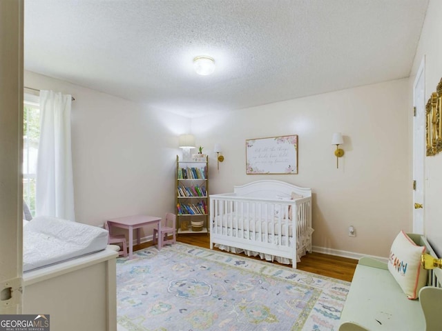 bedroom with a textured ceiling, a crib, wood finished floors, and baseboards