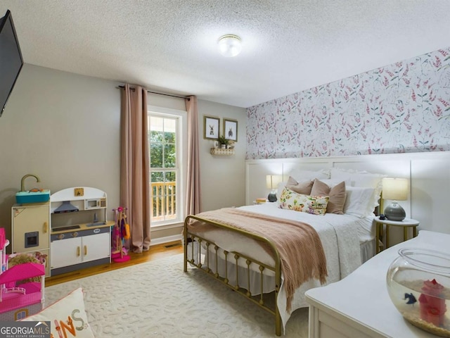 bedroom with a textured ceiling, visible vents, light wood-style flooring, and wallpapered walls