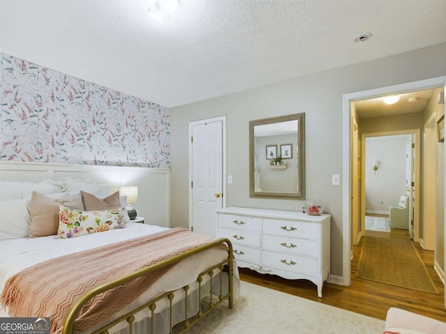 bedroom with a textured ceiling, wood finished floors, and wallpapered walls