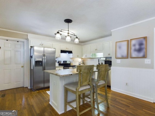 kitchen with dark wood-style floors, appliances with stainless steel finishes, white cabinets, a kitchen island, and under cabinet range hood