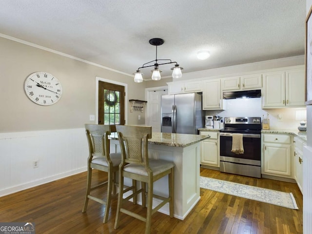 kitchen featuring under cabinet range hood, a wainscoted wall, stainless steel appliances, a kitchen breakfast bar, and dark wood finished floors