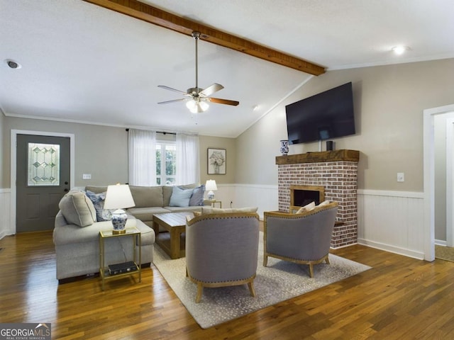 living area with a wainscoted wall, lofted ceiling with beams, a brick fireplace, and wood finished floors