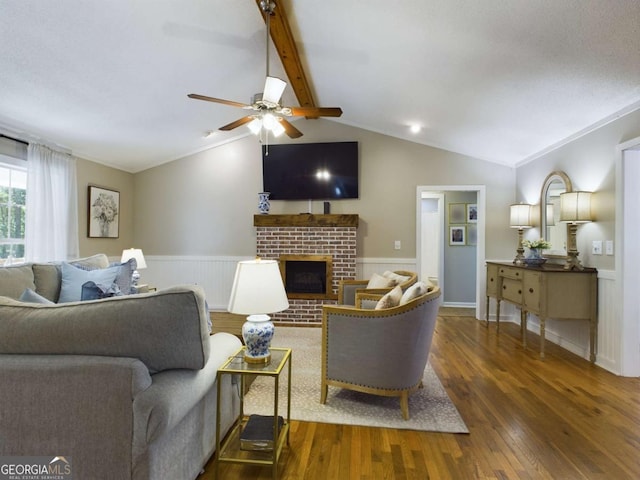 living room with vaulted ceiling with beams, ceiling fan, a brick fireplace, and wood finished floors