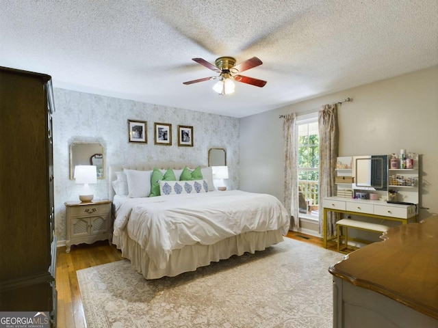 bedroom with wallpapered walls, a textured ceiling, a ceiling fan, and hardwood / wood-style floors