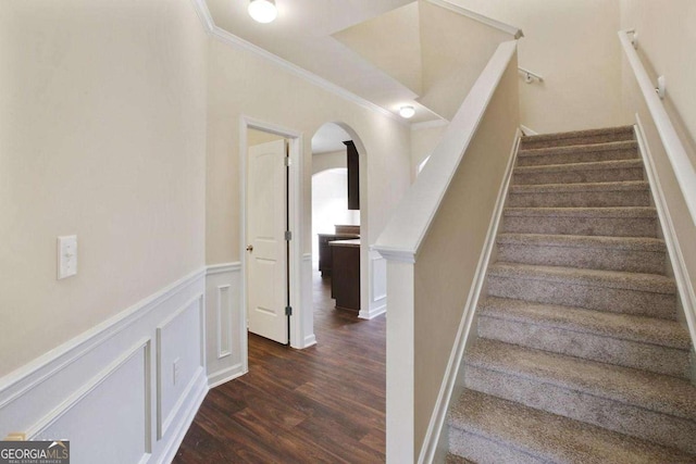 stairway featuring arched walkways, a decorative wall, wood finished floors, wainscoting, and crown molding