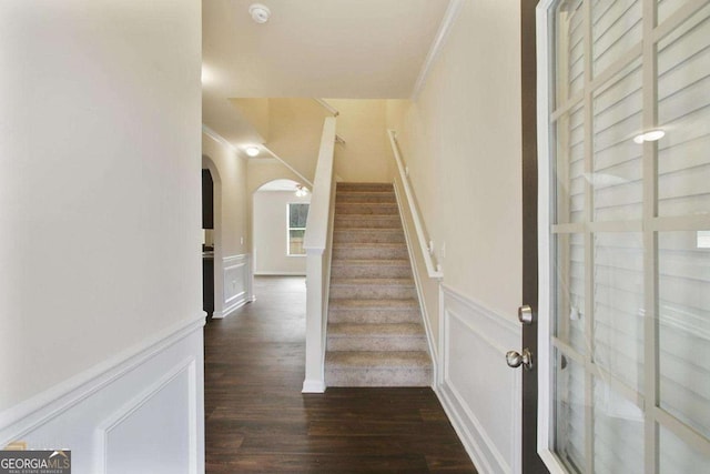 stairway featuring arched walkways, a decorative wall, ornamental molding, wainscoting, and wood finished floors