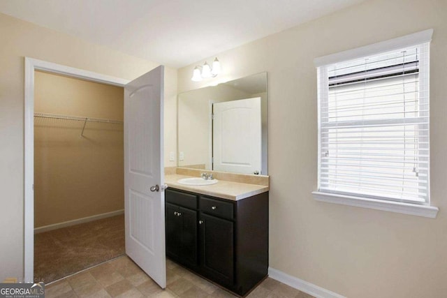 bathroom with baseboards, a walk in closet, and vanity